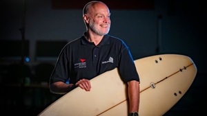Dr Brendon Ferrier holding a surf board